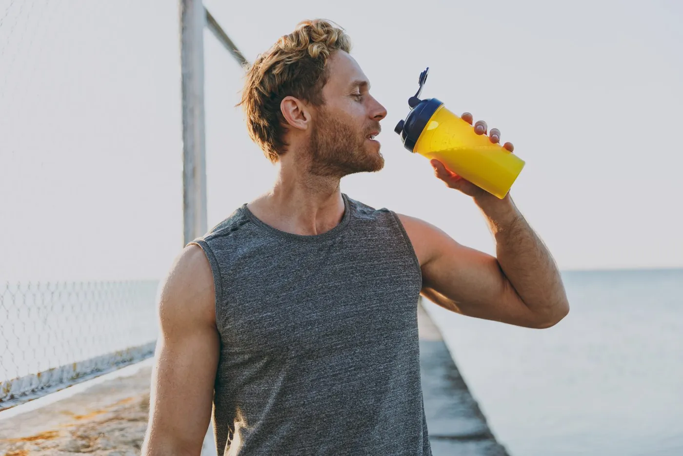 Mann trinkt am Meer aus einem gelben Shaker