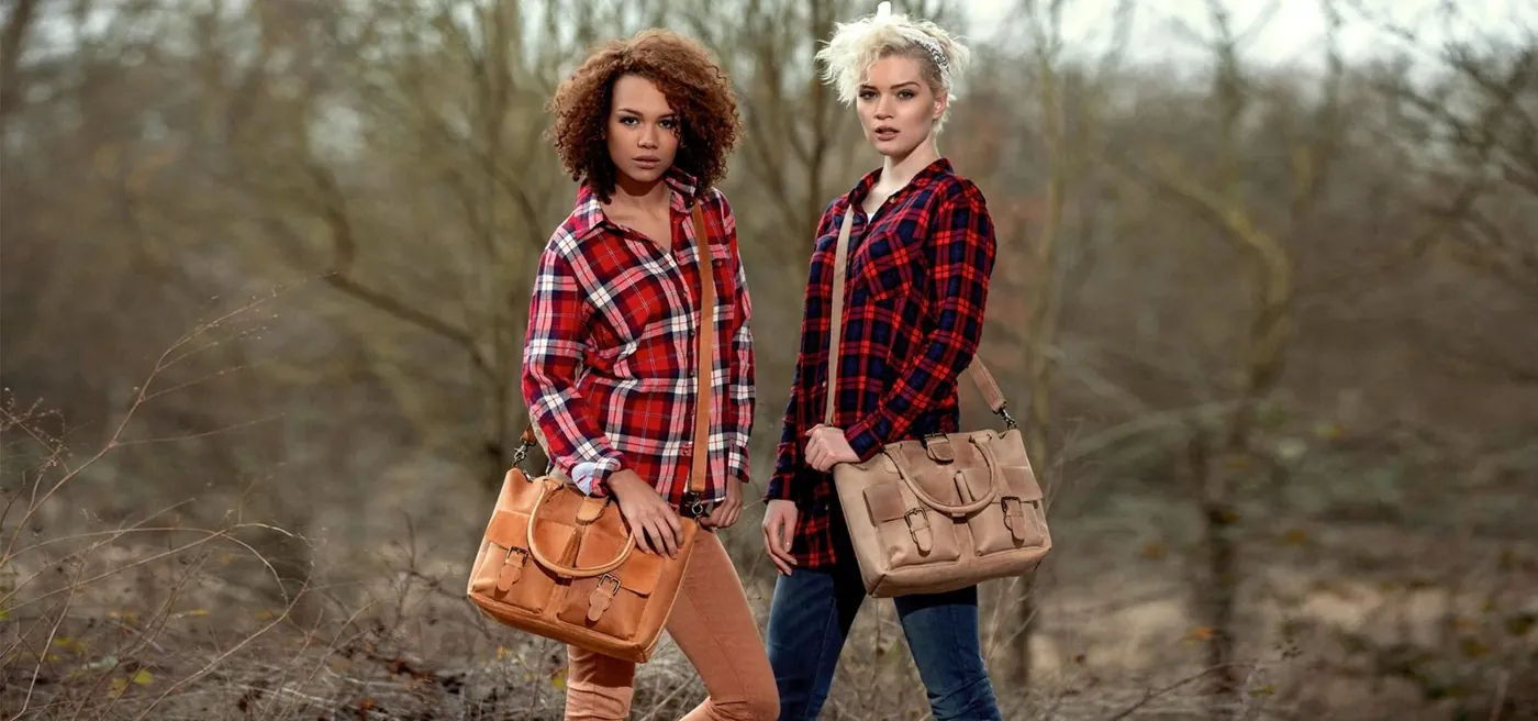 Zwei Frauen in Karohemden mit Ledertaschen im Wald