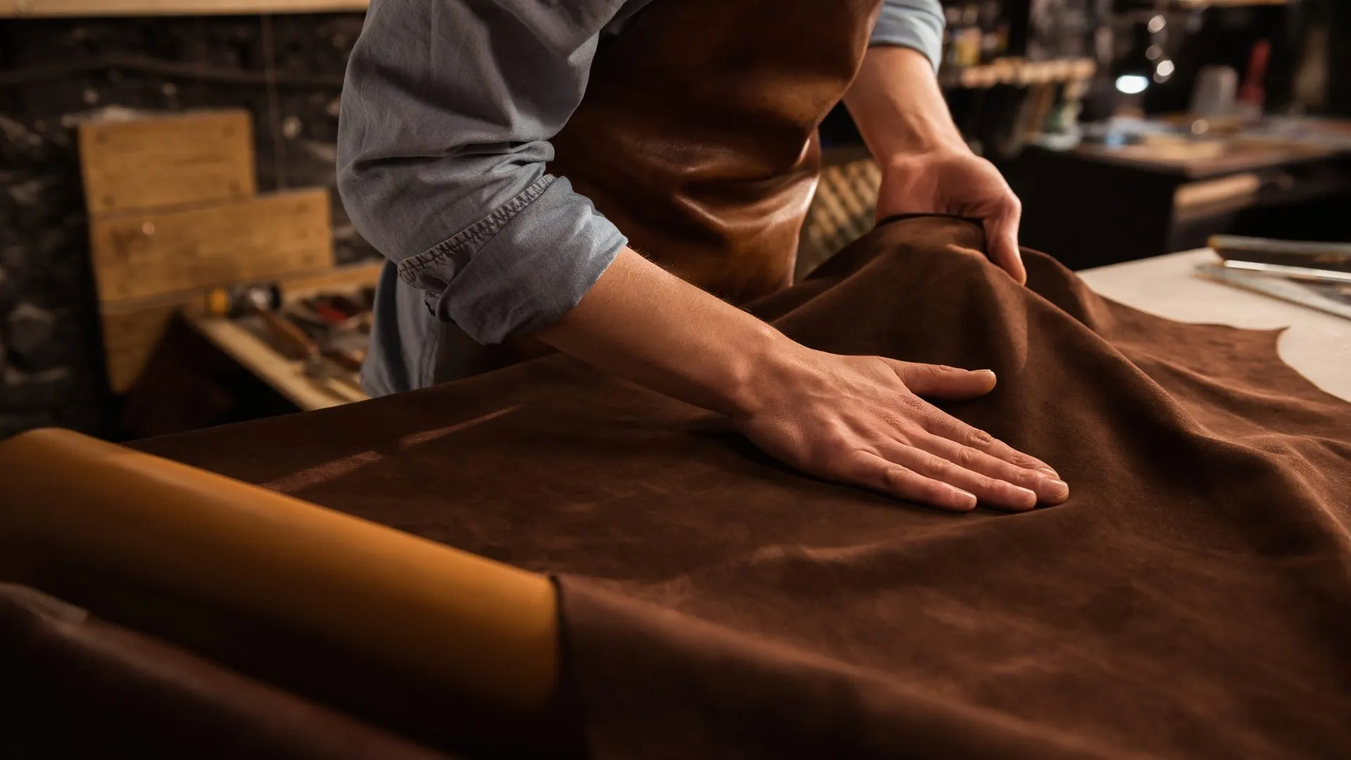 Hände glätten ein braunes Leder auf einem Werkstatttisch