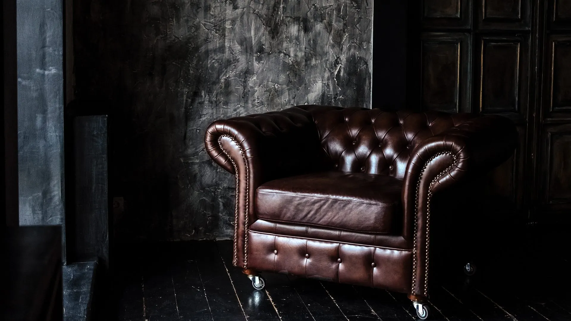 Brauner Chesterfield-Ledersessel vor einer dunklen Wand
